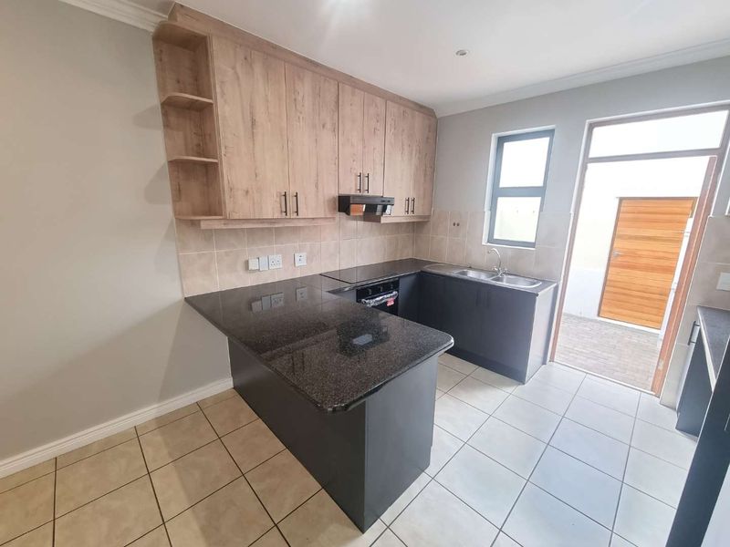 Modern kitchen featuring granite countertops, built-in cabinetry, integrated oven with extractor fan, and direct access to an outdoor area.