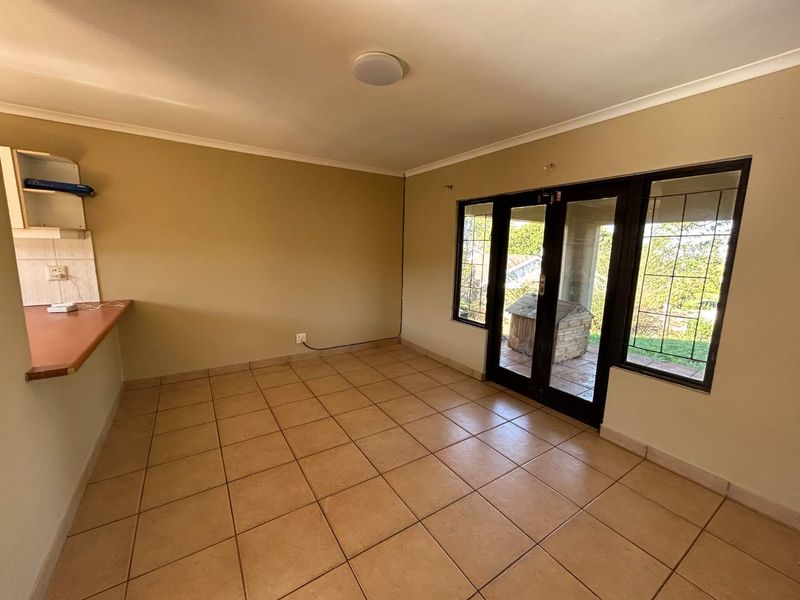 An empty open-plan living area featuring tiled flooring, a kitchen counter, and glass french doors leading to an outdoor patio.