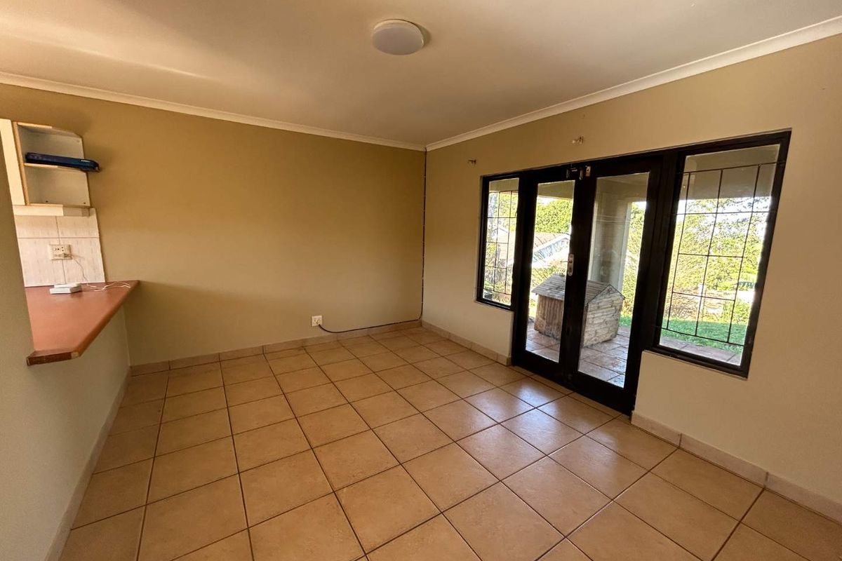An empty open-plan living area featuring tiled flooring, a kitchen counter, and glass french doors leading to an outdoor patio.