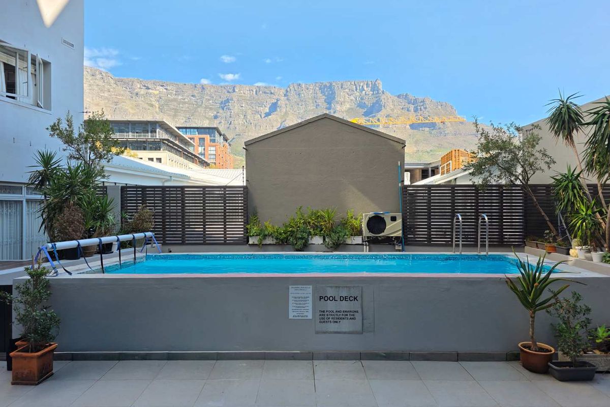 A well-maintained communal pool area featuring a tiled deck, slatted privacy fencing, and clear views of Table Mountain.