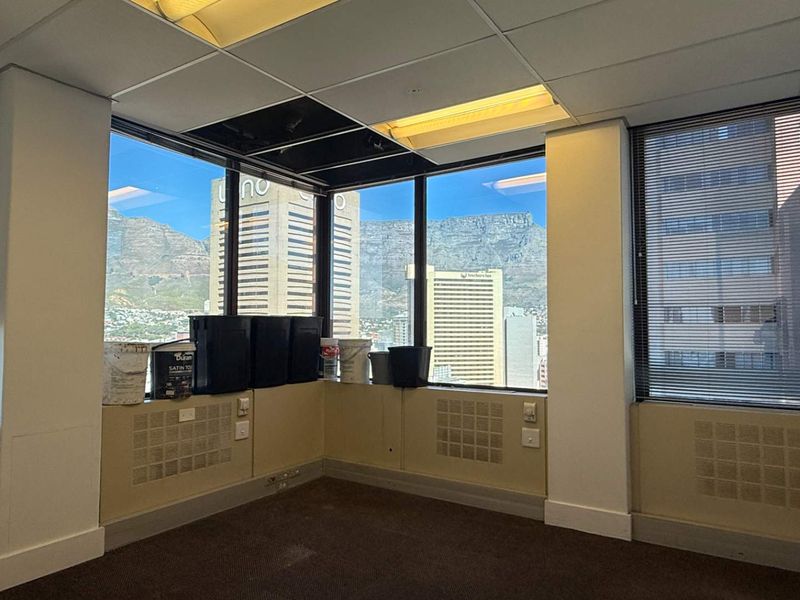 Empty office space featuring large windows with city and mountain views, suspended ceiling, and carpeted flooring.