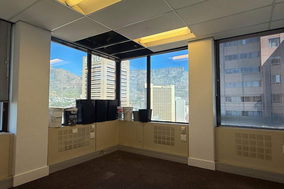 Empty office space featuring large windows with city and mountain views, suspended ceiling, and carpeted flooring.
