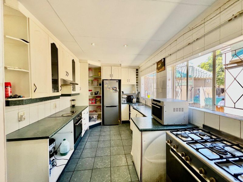 Functional kitchen featuring ample built-in cabinetry, tiled flooring, a built-in oven, hob, and extractor fan, with large windows providing natural light.