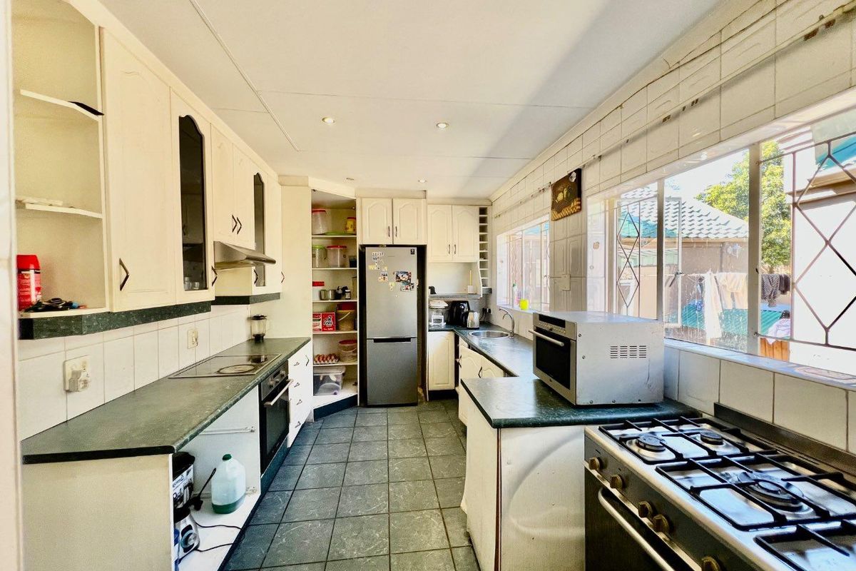 Functional kitchen featuring ample built-in cabinetry, tiled flooring, a built-in oven, hob, and extractor fan, with large windows providing natural light.