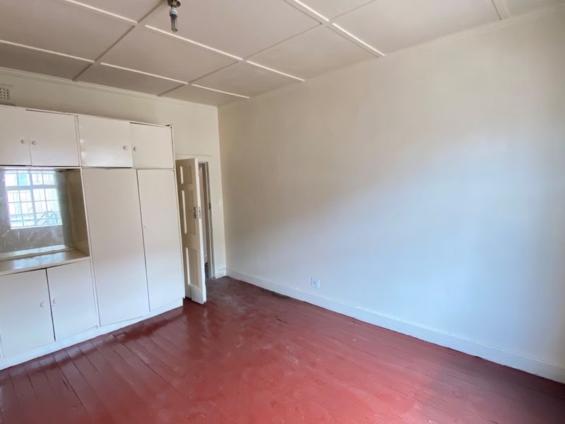 An empty bedroom featuring original timber flooring, built-in cupboards, and a tiled ceiling, offering a blank canvas for renovation or restyling.