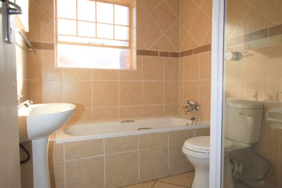 A functional bathroom featuring a pedestal basin, built-in bathtub, toilet, and a separate shower enclosure with neutral ceramic tiling throughout.