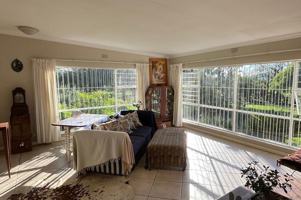 Spacious living room featuring large windows with security bars, tiled flooring, and abundant natural light overlooking the garden.