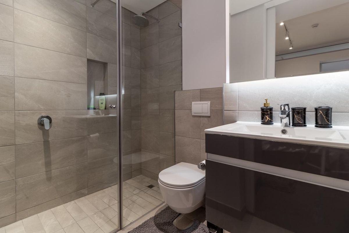 Modern bathroom featuring a glass-enclosed walk-in shower with tiled niche, wall-mounted toilet, and a sleek vanity unit with integrated lighting.