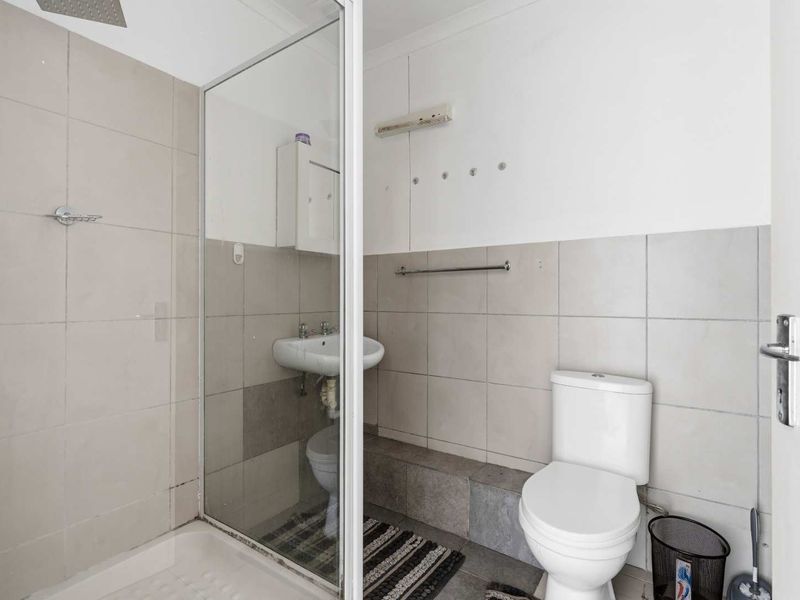 A functional bathroom featuring a shower enclosure, wall-mounted basin, and toilet with neutral wall tiling.