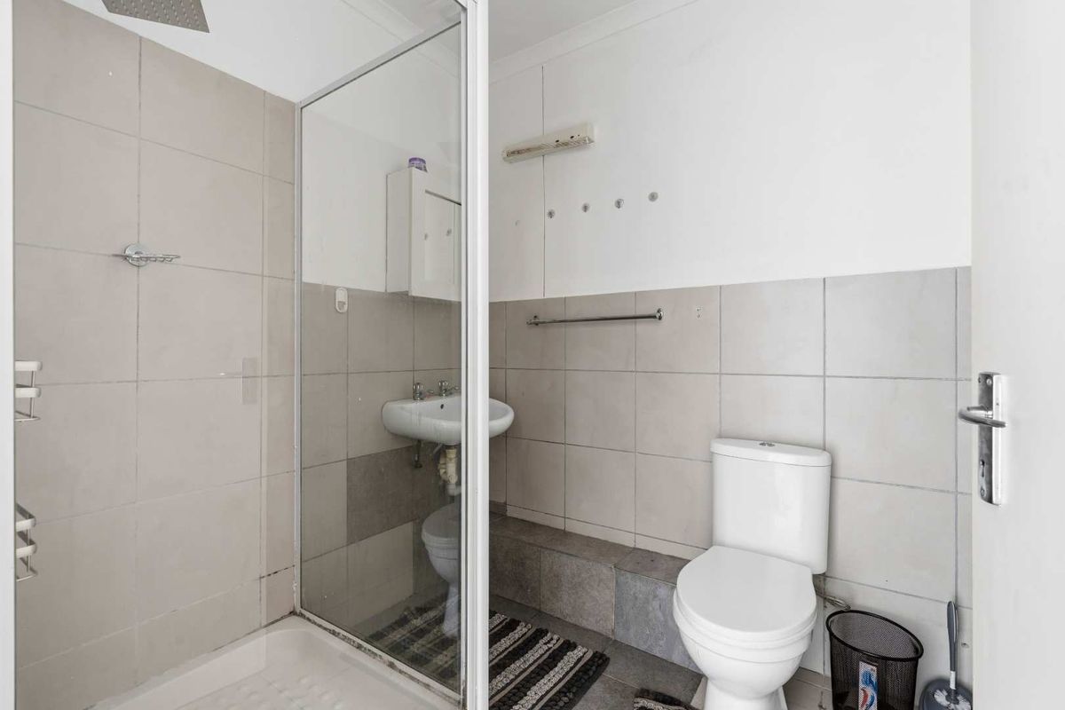 A functional bathroom featuring a shower enclosure, wall-mounted basin, and toilet with neutral wall tiling.