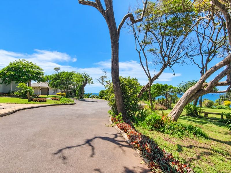 A spacious asphalt driveway leading to the front entrance of a cluster home, featuring landscaped gardens and scenic coastal views.