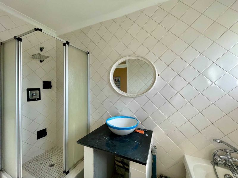 A bathroom featuring a shower enclosure with a rain shower head, a vessel sink on a stone vanity top, and diamond-patterned wall tiles.