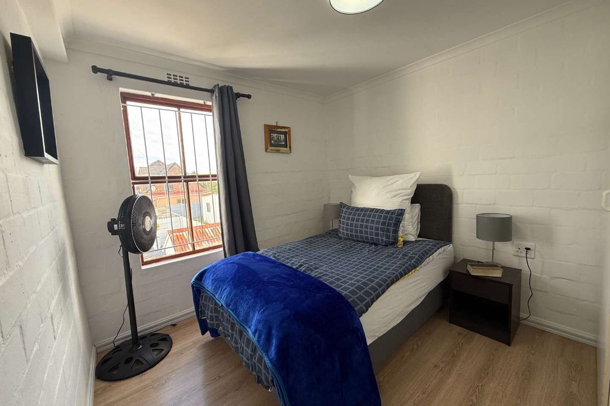 A compact bedroom featuring painted brick walls, laminate flooring, and a window fitted with security bars.