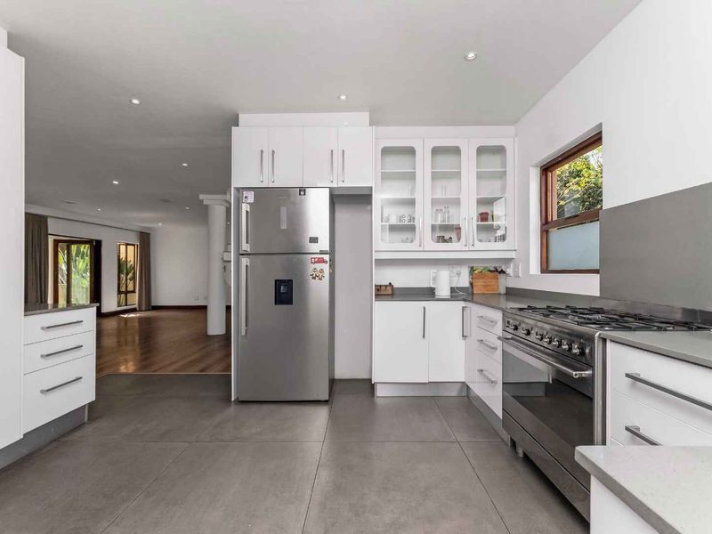 Modern kitchen featuring white cabinetry, stone countertops, a gas range, and large format floor tiles, seamlessly flowing into the adjacent living area.