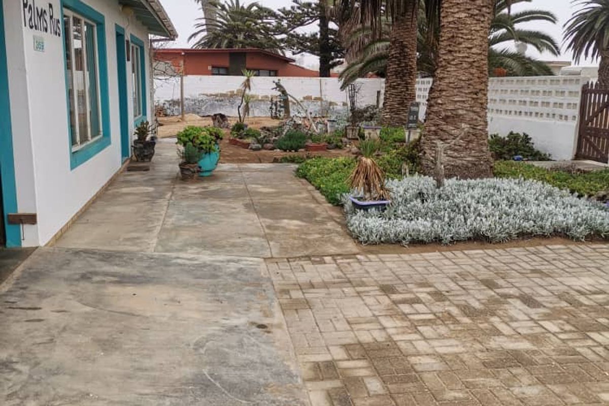 A view of the side exterior area featuring paved walkways, established palm trees, and a low boundary wall.