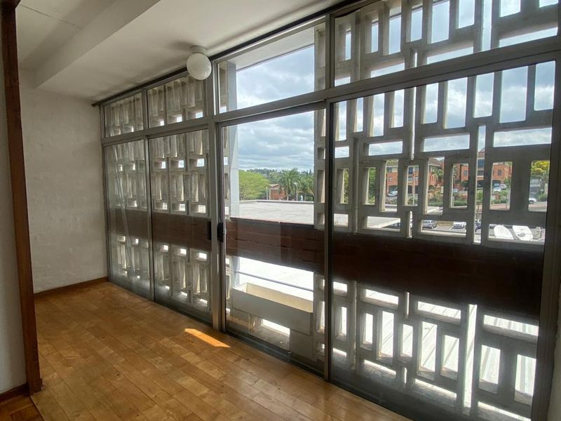 An enclosed balcony or sunroom featuring distinctive decorative concrete breeze block screens, sliding glass doors, and original parquet flooring.