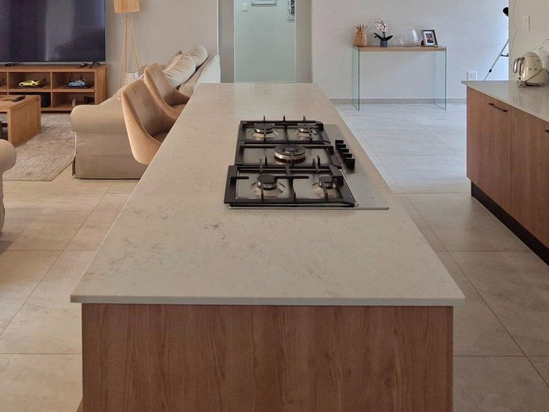 Modern open-plan living area featuring a central kitchen island with a built-in gas hob and stone countertops, seamlessly integrated with the living space.
