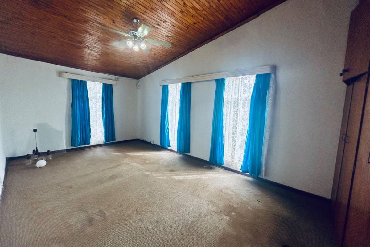 Spacious bedroom featuring a vaulted timber-clad ceiling, ceiling fan, and large windows with natural light.