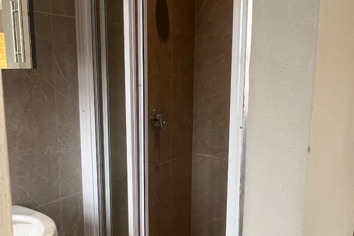 A compact bathroom featuring a tiled shower enclosure with a glass door and a wall-mounted basin.