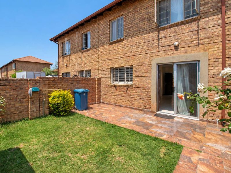 Rear view of the townhouse featuring a private garden, tiled patio area, and direct access to the interior through a sliding glass door.