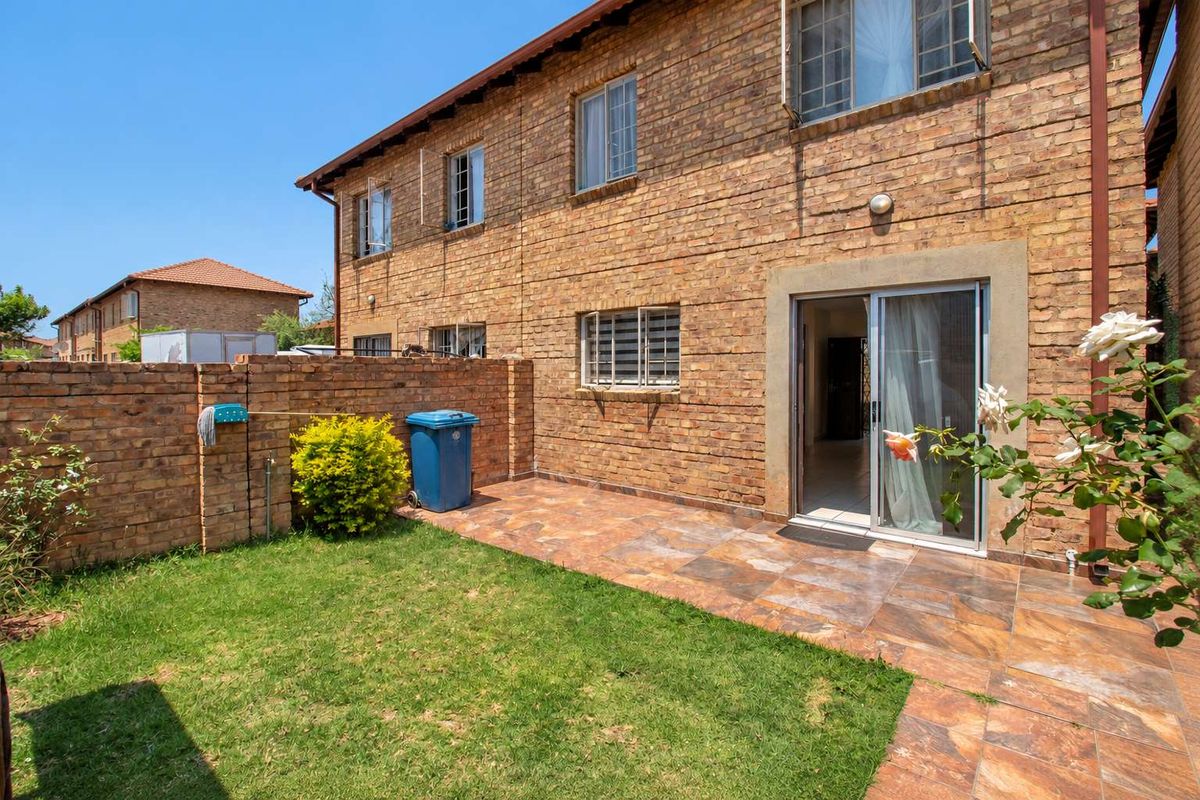 Rear view of the townhouse featuring a private garden, tiled patio area, and direct access to the interior through a sliding glass door.