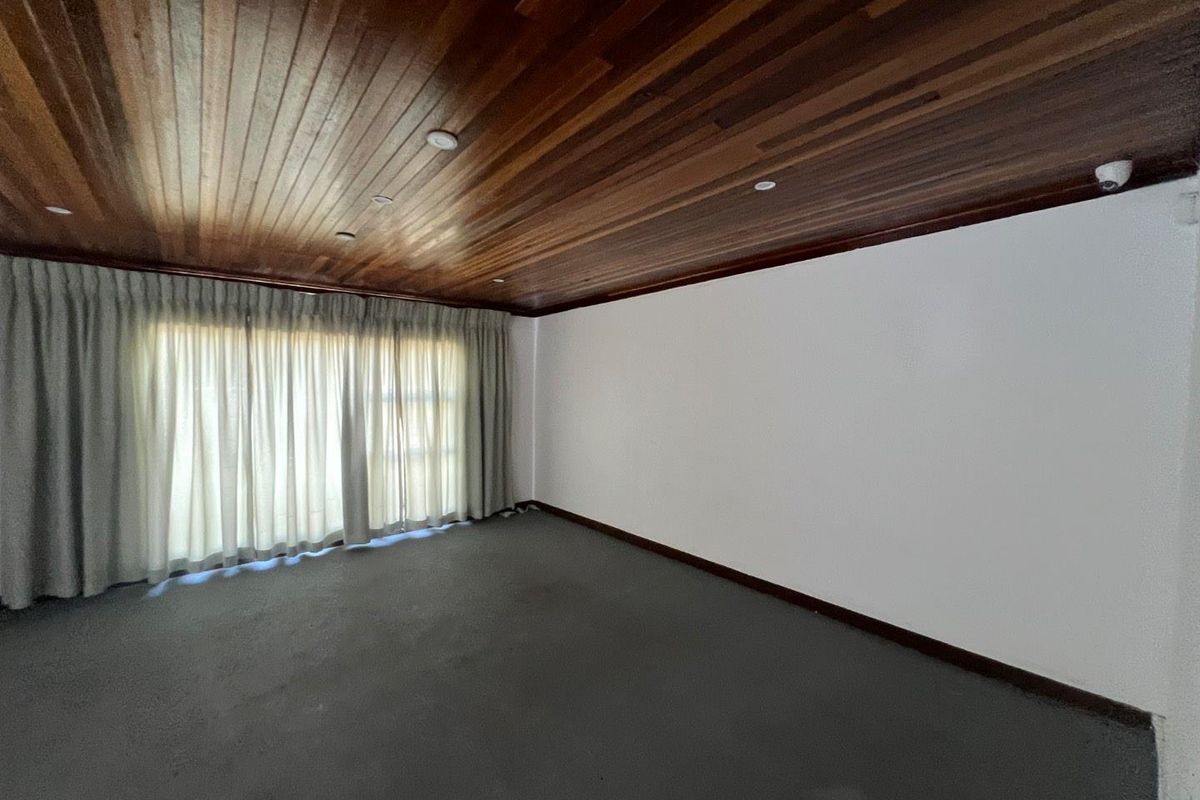 A spacious, empty living room featuring a distinctive timber-paneled ceiling, neutral walls, and large sliding glass doors with integrated curtain tracks.