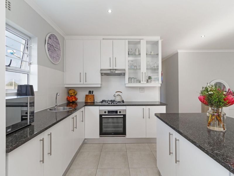 Modern kitchen featuring white cabinetry, granite countertops, built-in oven, gas hob, extractor fan, and tiled flooring with ample storage space.