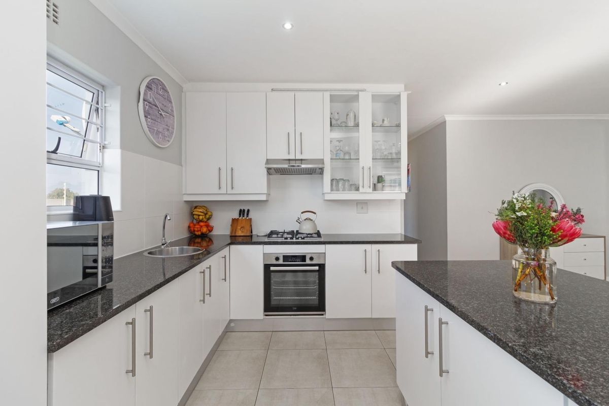 Modern kitchen featuring white cabinetry, granite countertops, built-in oven, gas hob, extractor fan, and tiled flooring with ample storage space.