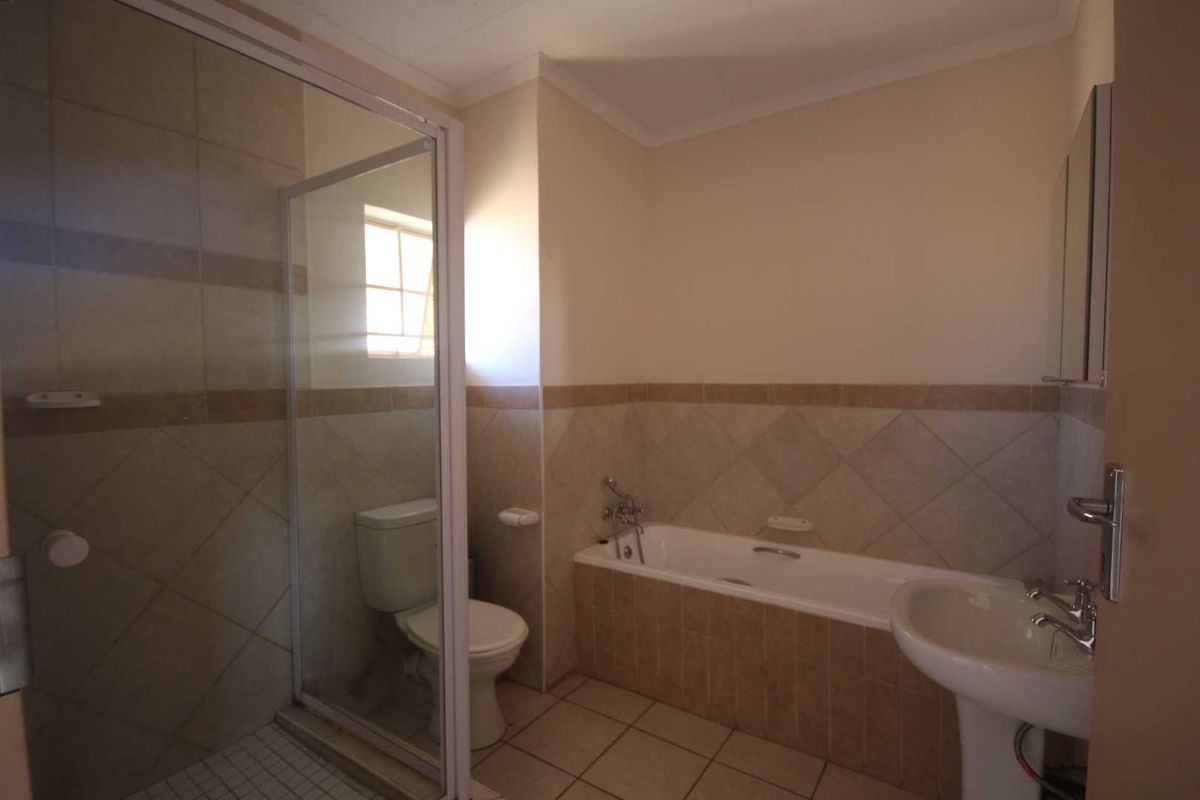 A functional bathroom featuring a separate shower enclosure, bathtub, pedestal basin, and toilet with neutral wall and floor tiling.