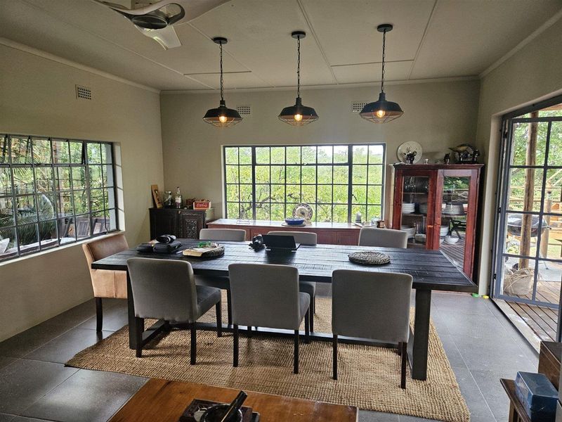 Spacious dining room featuring large steel-framed windows, modern pendant lighting, and tiled flooring with direct access to an outdoor deck area.