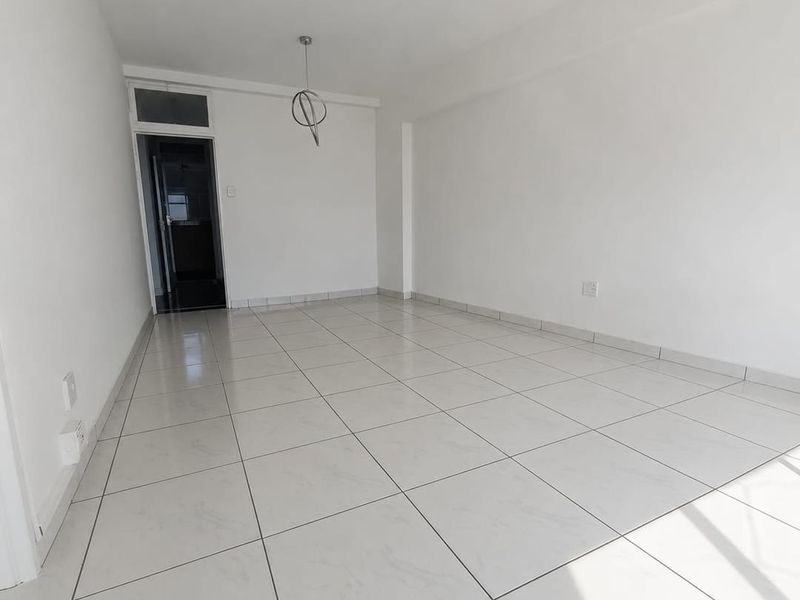 A bright, empty living area featuring neutral tiled flooring and modern pendant light fittings, ready for personalization.