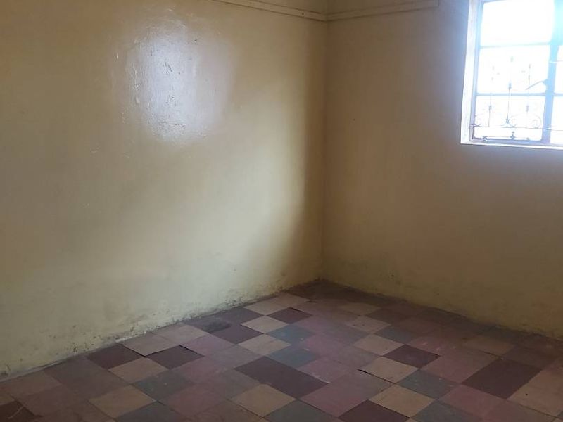 An empty bedroom featuring worn checkered floor tiles and plain walls, requiring cosmetic updates and flooring replacement to restore its appeal.