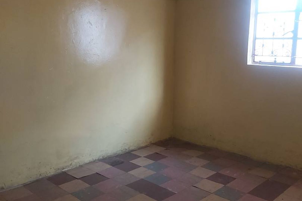 An empty bedroom featuring worn checkered floor tiles and plain walls, requiring cosmetic updates and flooring replacement to restore its appeal.