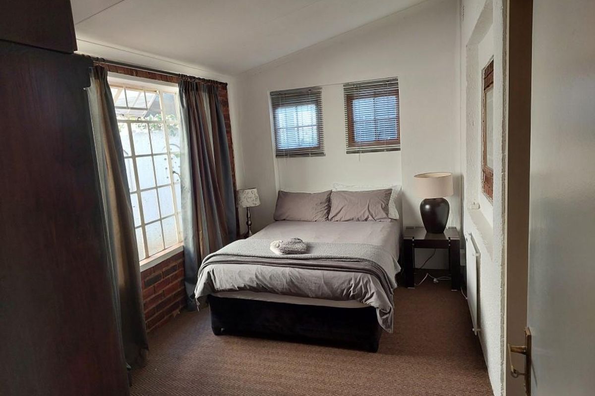 A cozy bedroom featuring exposed brick accents, dual windows with blinds, and neutral carpeting.