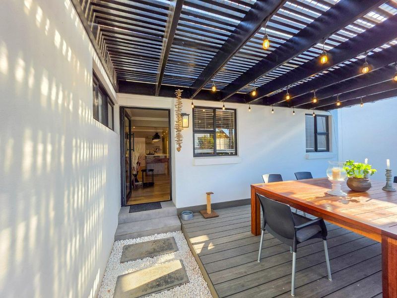A well-maintained covered patio featuring timber decking, a modern pergola structure with integrated string lighting, and direct access to the home interior.