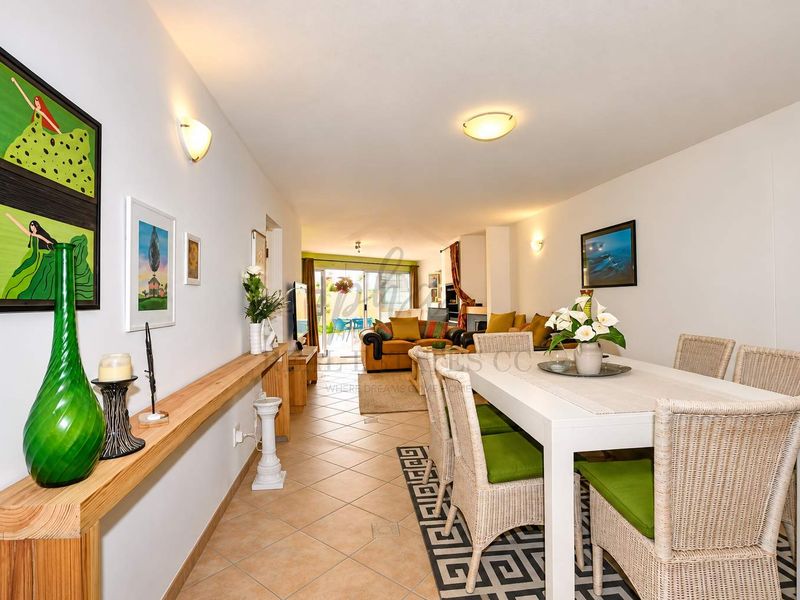 Open-plan living and dining area featuring tiled flooring, a wall-mounted wooden console shelf, and sliding glass doors leading to an outdoor patio space.