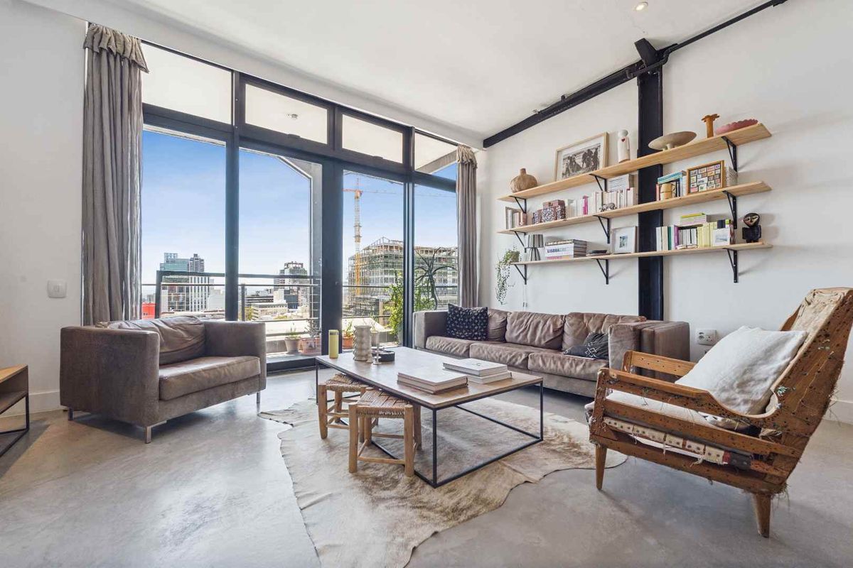 A bright, modern living room featuring polished concrete floors, an exposed structural column, and expansive floor-to-ceiling windows with access to a balcony.