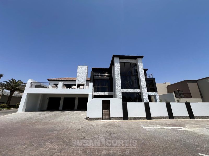 Modern multi-story residence featuring a triple garage, stone-clad facade, expansive glass windows, and a private balcony, set behind a secure perimeter wall.