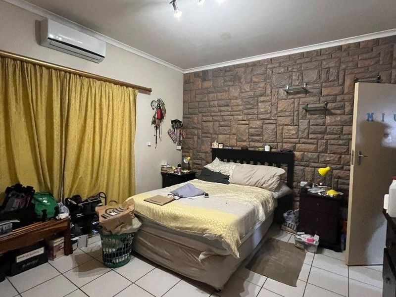 A bedroom featuring a stone-cladding accent wall, ceramic tiled flooring, and a wall-mounted air conditioning unit.
