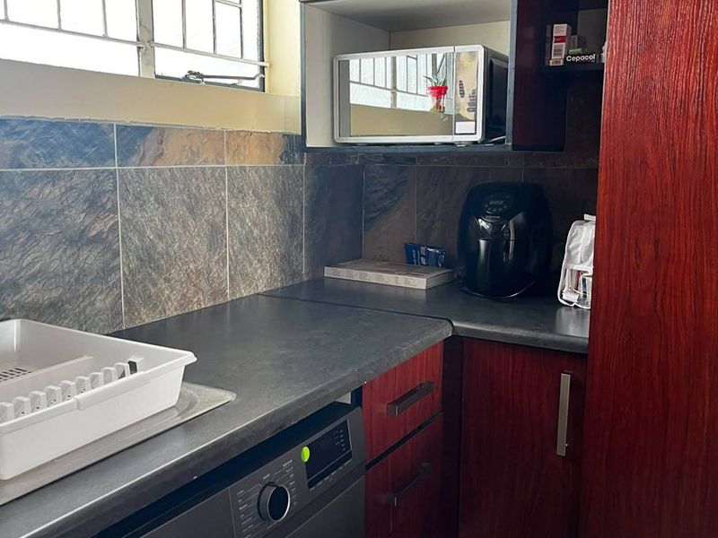 Compact laundry area featuring dark wood-look cabinetry, stone-effect tiled backsplash, laminate countertops, and a built-in washing machine.
