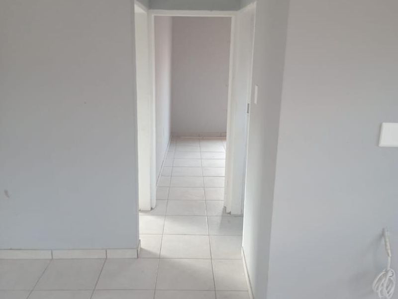 A neutral-toned hallway featuring ceramic floor tiles, white skirting boards, and crown molding, providing a clean and simple transition between living spaces.