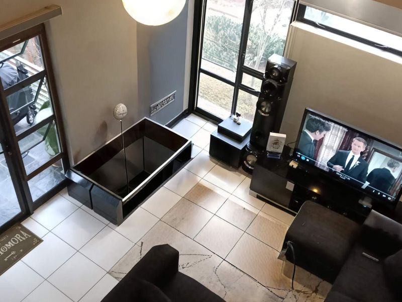 A high-angle view of a modern living room featuring tiled floors, large glass doors leading to a balcony, and a spacious double-volume layout.