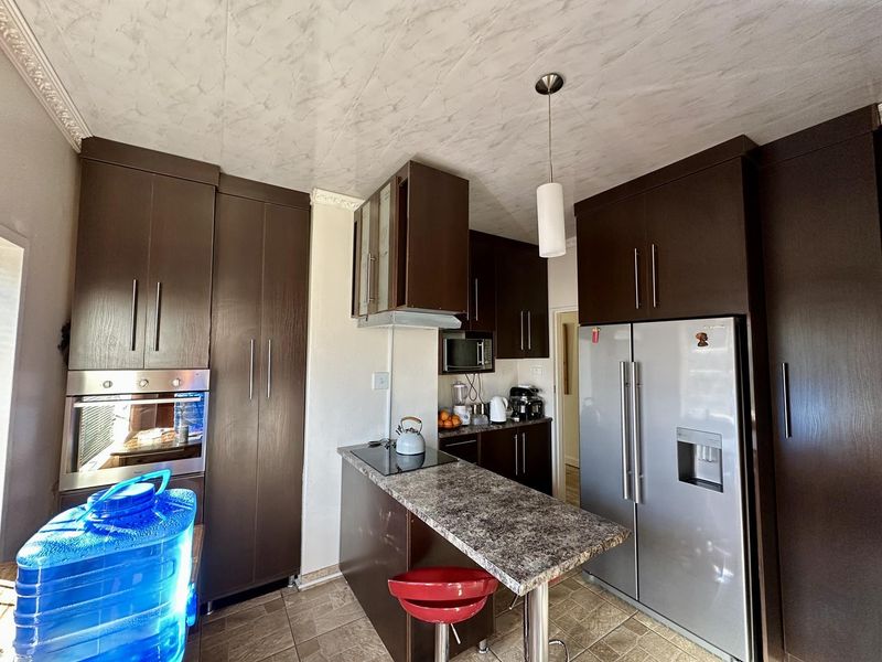 A compact kitchen featuring dark wood-finish cabinetry, a breakfast bar with laminate countertop, built-in oven, and tiled flooring.