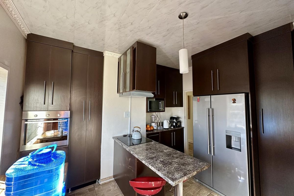 A compact kitchen featuring dark wood-finish cabinetry, a breakfast bar with laminate countertop, built-in oven, and tiled flooring.