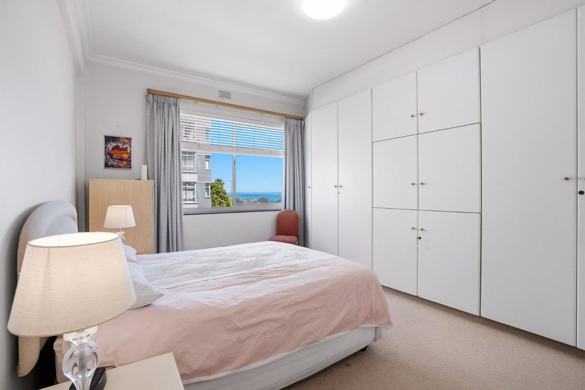 A well-maintained bedroom featuring extensive floor-to-ceiling built-in wardrobes, neutral carpeting, and a window offering a pleasant view.