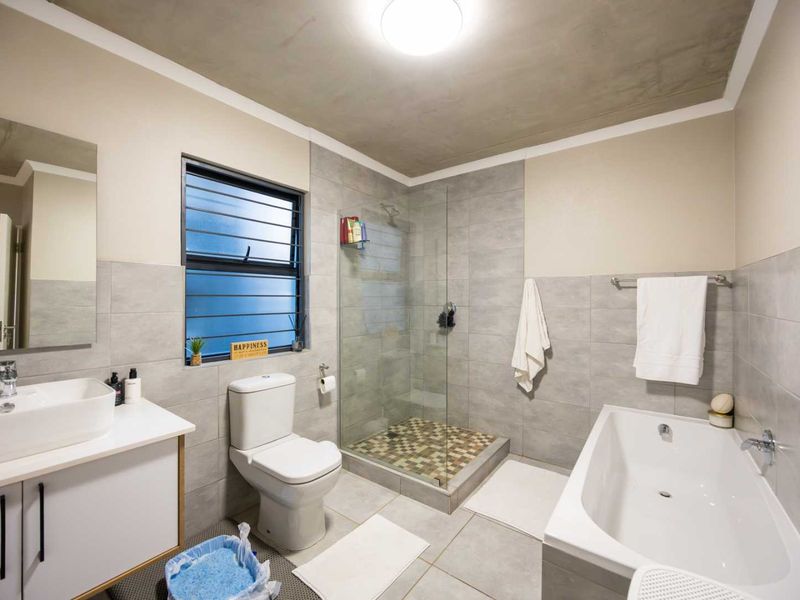 Modern bathroom featuring a glass-enclosed shower, separate bathtub, vessel sink vanity, and neutral grey tiling throughout.