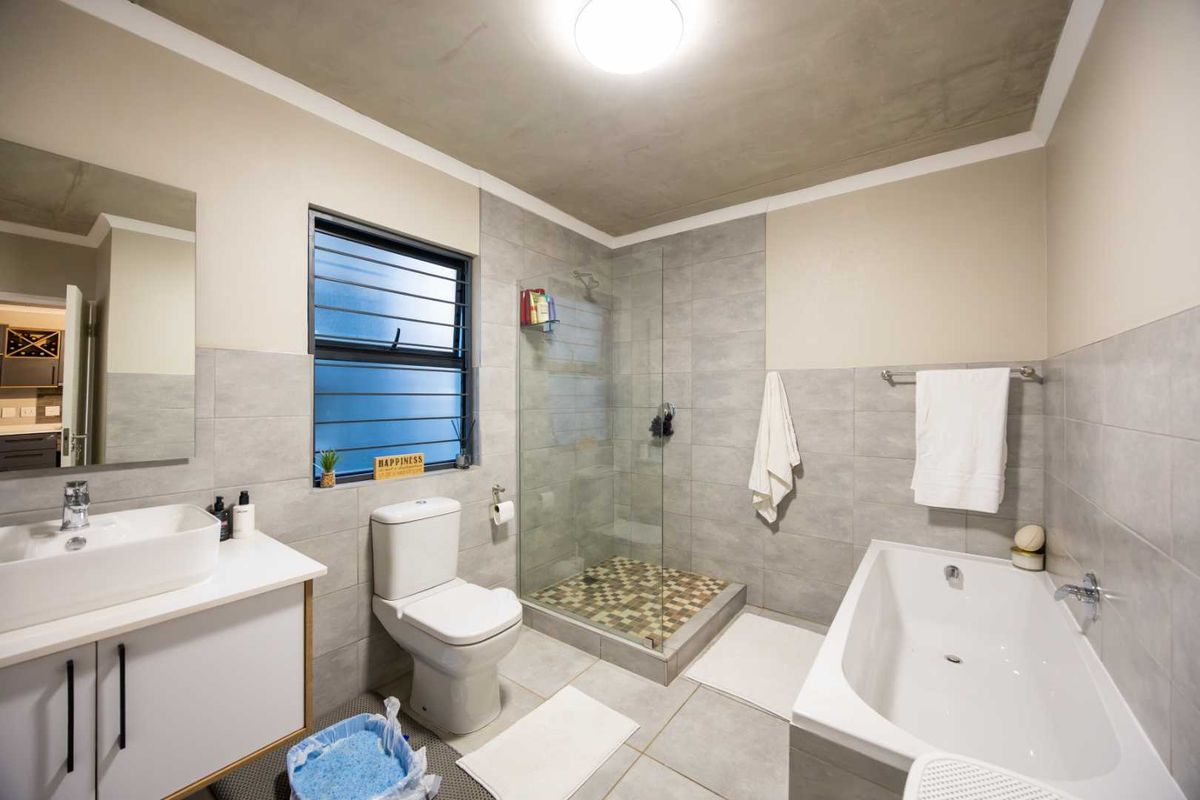 Modern bathroom featuring a glass-enclosed shower, separate bathtub, vessel sink vanity, and neutral grey tiling throughout.