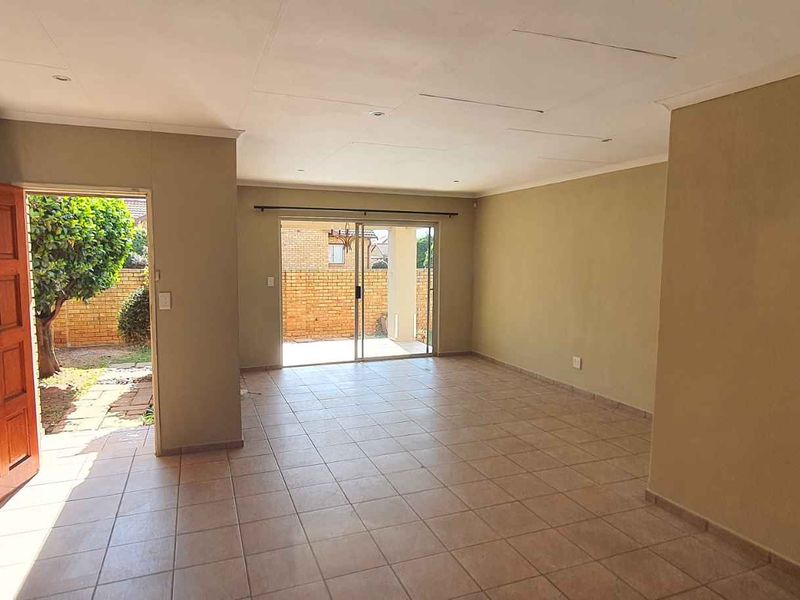 Spacious, empty living area featuring tiled flooring, a wooden entrance door, and sliding glass doors leading to the rear exterior.