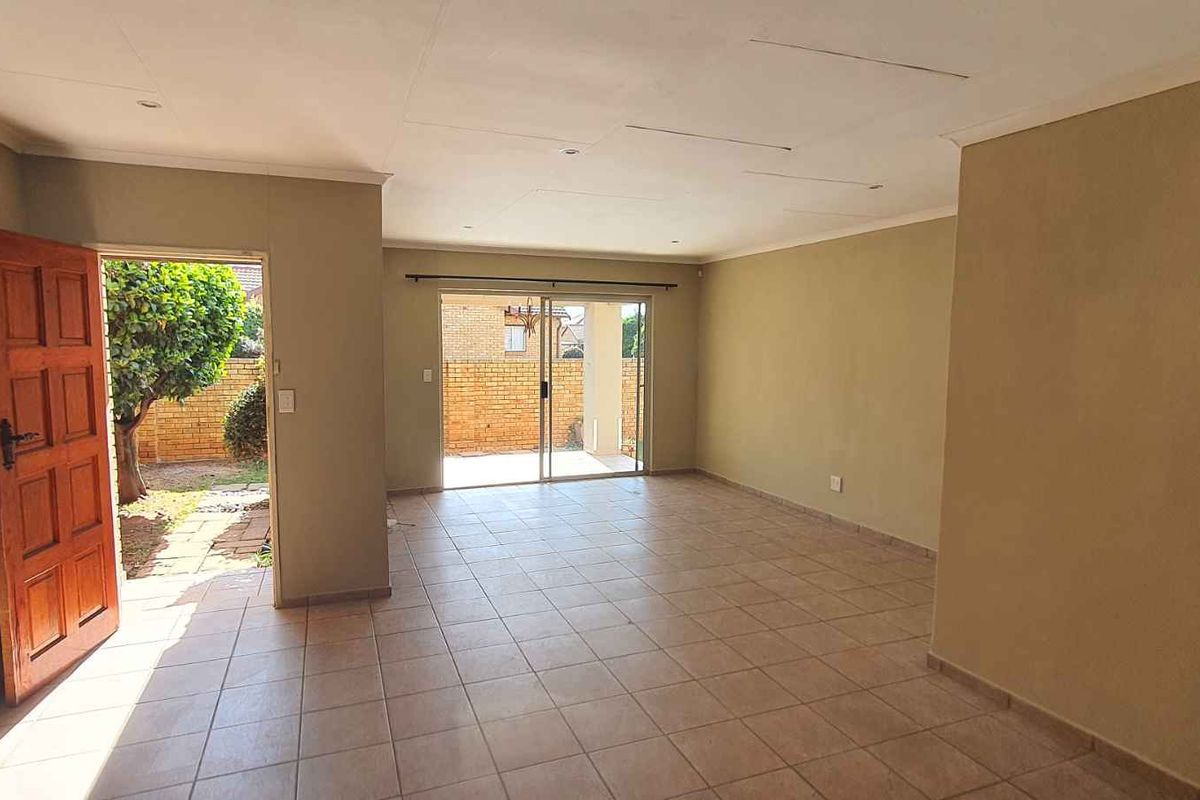 Spacious, empty living area featuring tiled flooring, a wooden entrance door, and sliding glass doors leading to the rear exterior.
