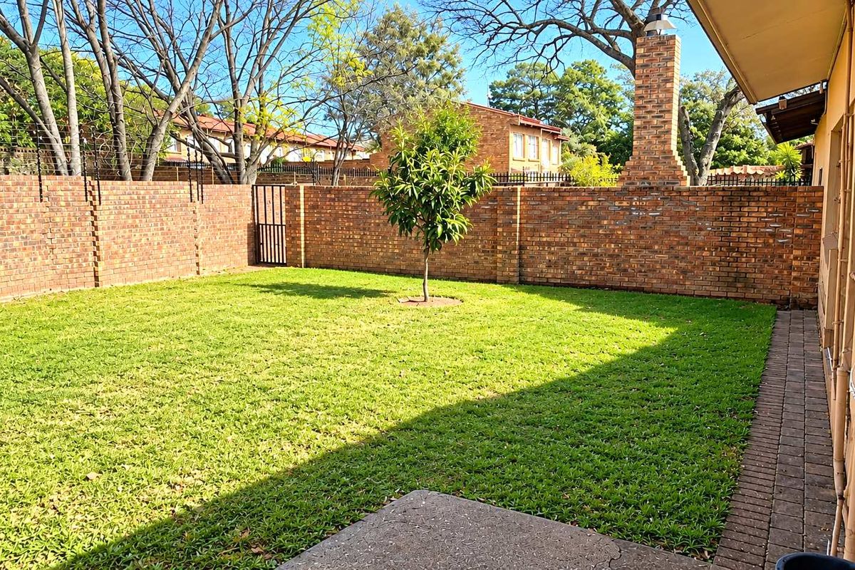 A private rear garden featuring a well-maintained lawn, brick boundary walls with electric fencing, and a prominent brick chimney.